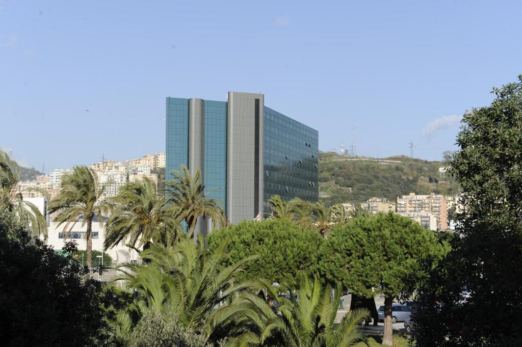 un grand bâtiment avec des palmiers en face d'une ville dans l'établissement Tower Genova Airport - Hotel & Conference Center, à Gênes