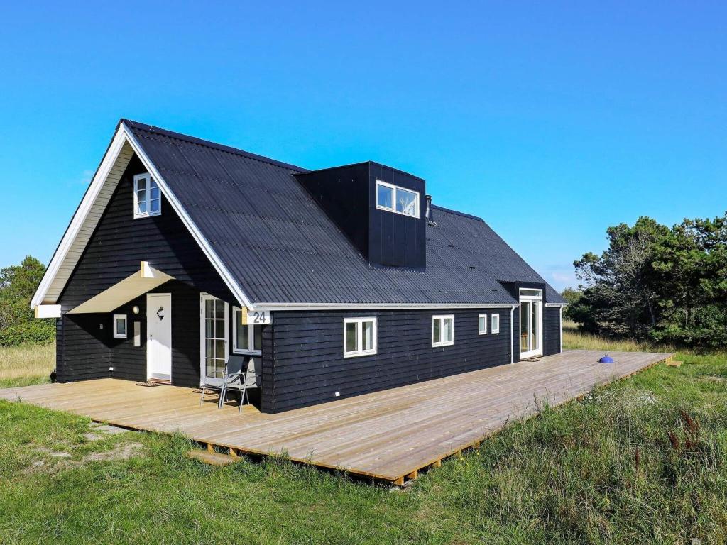 a black house with a wooden deck in a field at 10 person holiday home in Skagen in Skagen