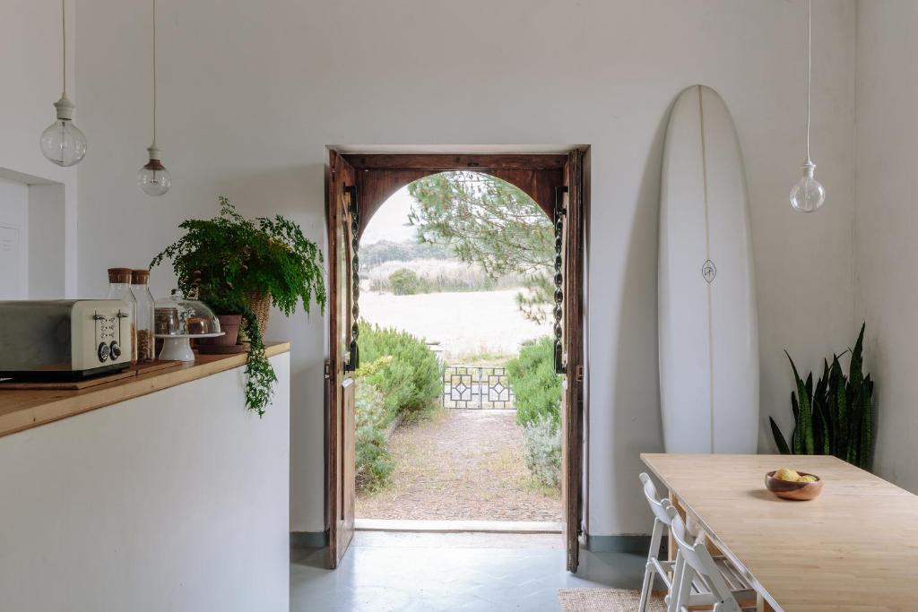an open door in a kitchen with a table and a surfboard at Cabeca Da Cabra Casa De Campo in Porto Covo