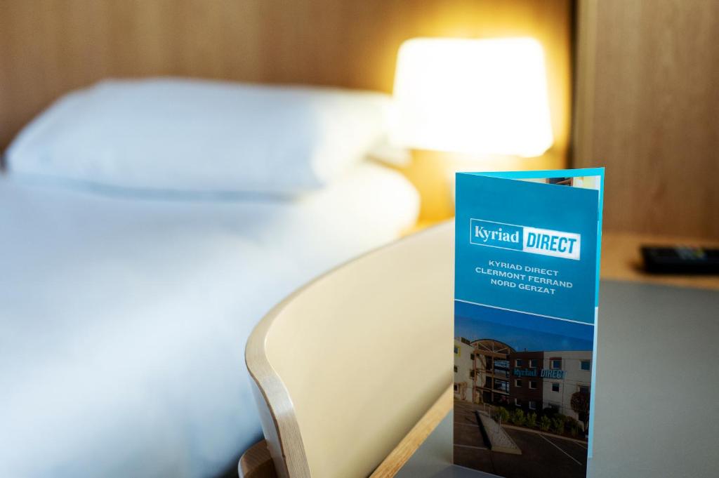 a hotel direct sign on a table next to a bed at Kyriad Direct Clermont Ferrand Nord Gerzat in Gerzat