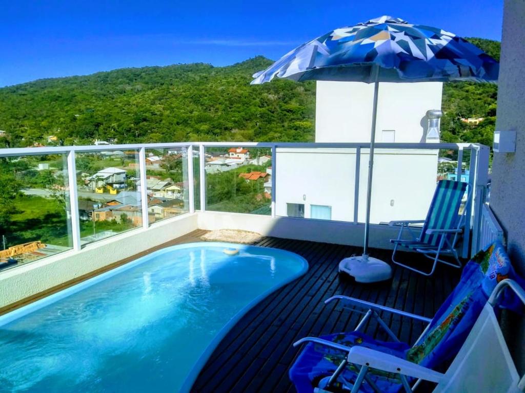 a balcony with a swimming pool and an umbrella and chairs at Linda Cobertura com Piscina - Conforto e Sofisticação! in Bombinhas