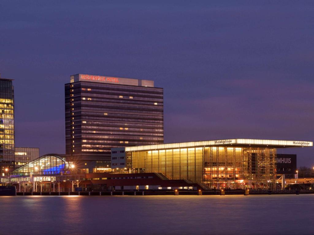 un grand bâtiment éclairé la nuit dans une ville dans l'établissement Mövenpick Hotel Amsterdam City Centre, à Amsterdam