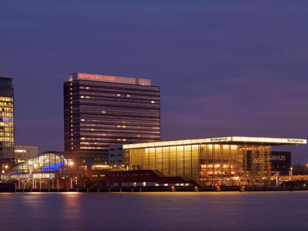 a large building with lights on in a city at night at Mövenpick Hotel Amsterdam City Centre in Amsterdam