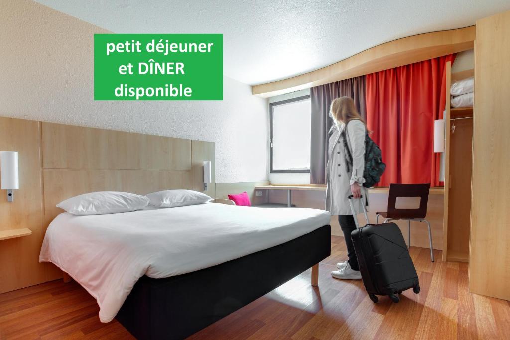 uma mulher ao lado de uma cama com uma mala em ibis Angers Centre Chateau em Angers