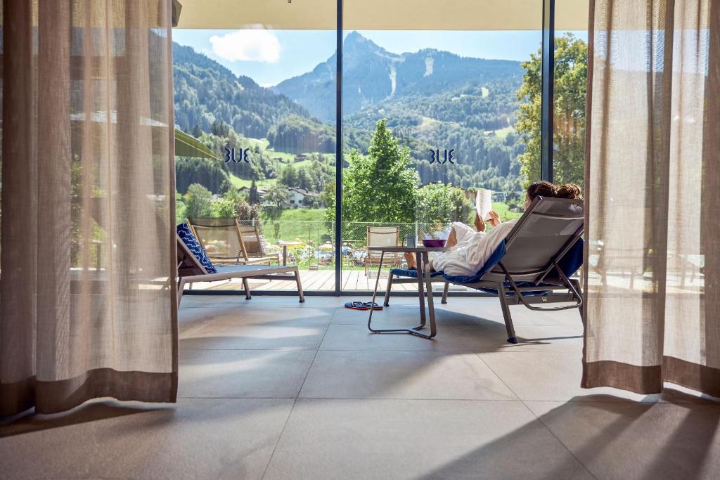 a woman sitting in a chair on a balcony looking out at the mountains at TUI BLUE Montafon in Schruns-Tschagguns