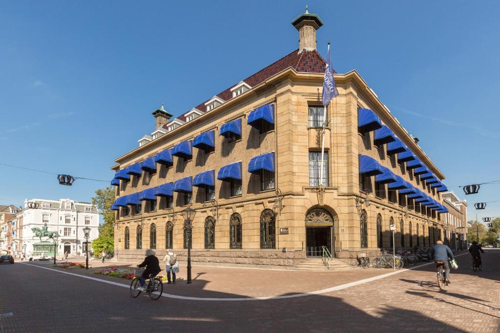 een gebouw met mensen die fietsen voor de deur bij Hotel Indigo The Hague - Palace Noordeinde, an IHG Hotel in Den Haag