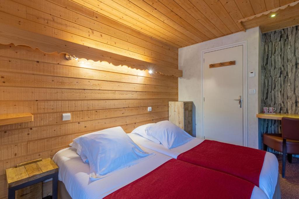 a bed in a room with a wooden wall at Hôtel Les Côtes, Résidence Loisirs et Chalets in Morzine
