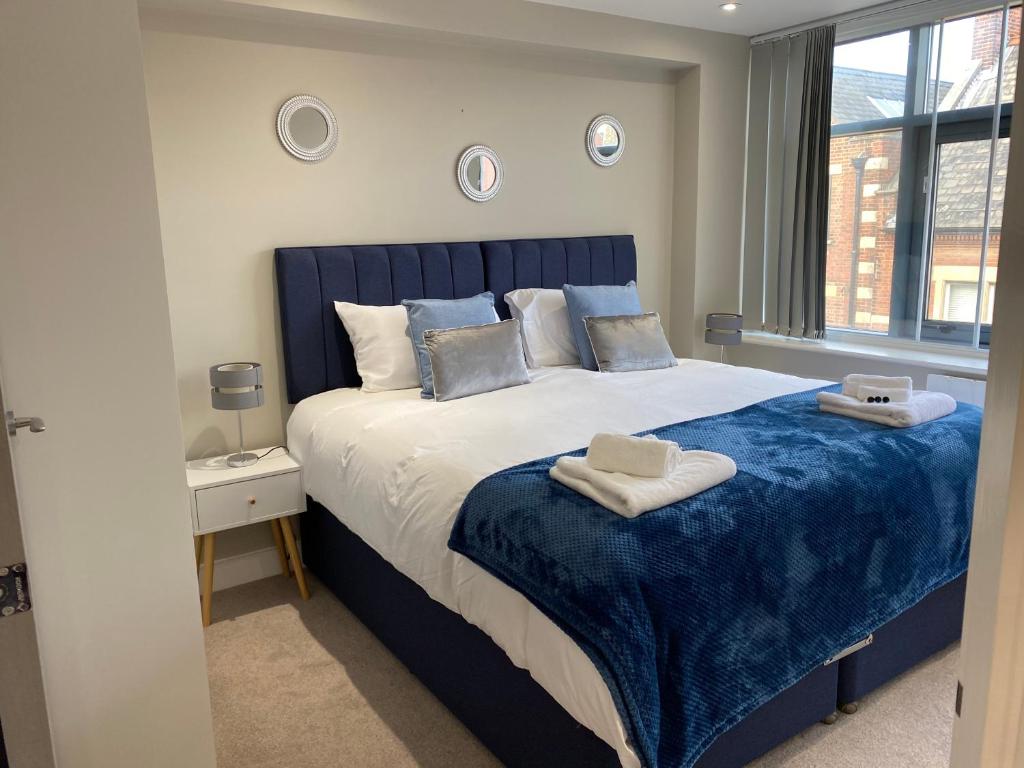 a bedroom with a blue and white bed with a window at Marie’s Serviced Apartment 1 Bed CityStay, parking in Bedford