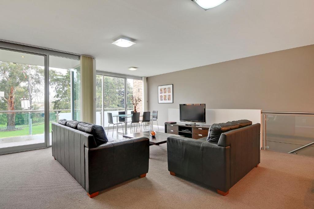 sala de estar con 2 sillas de cuero y TV en Traralgon Serviced Apartments, en Traralgon