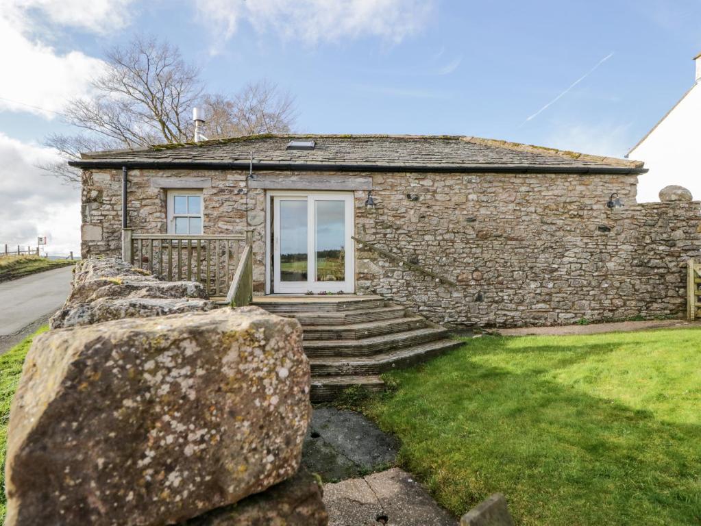 a stone house with a stone wall in the grass at The Cow House in Penrith