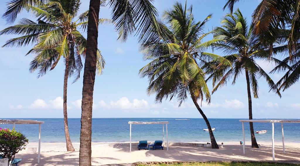 a beach with two palm trees and a gazebo at Diwani Cottage in Malindi