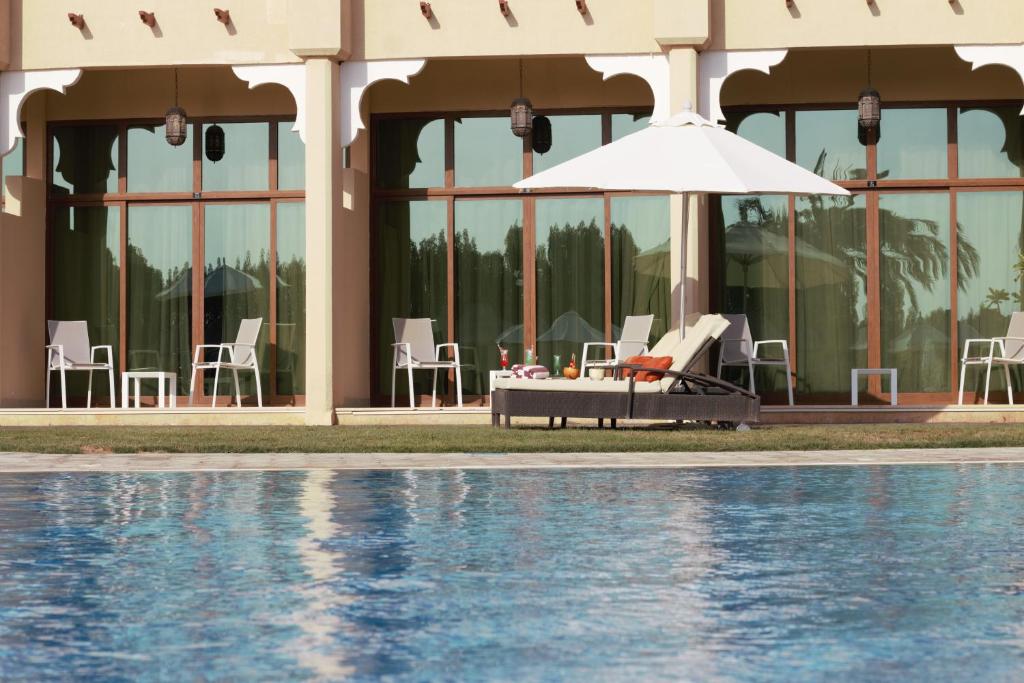 マディナ・ザイードにあるWestern Hotel - Madinat Zayedの建物の隣にプール(椅子、パラソル付)