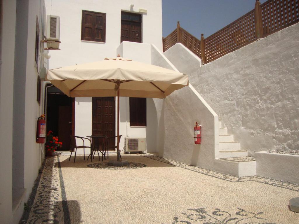 een patio met een parasol, een tafel en een trap bij Sarris Studios & Apartments in Lindos