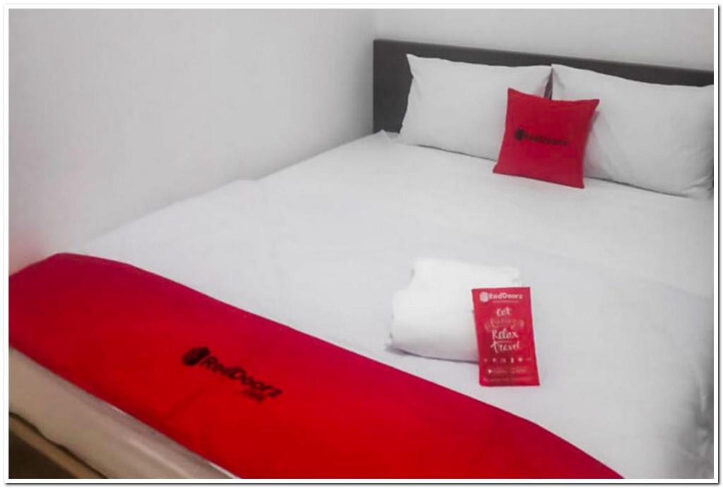 uma cama branca com um cobertor vermelho e almofadas vermelhas em RedDoorz near Moro Mall Purwokerto 2 em Purwokerto