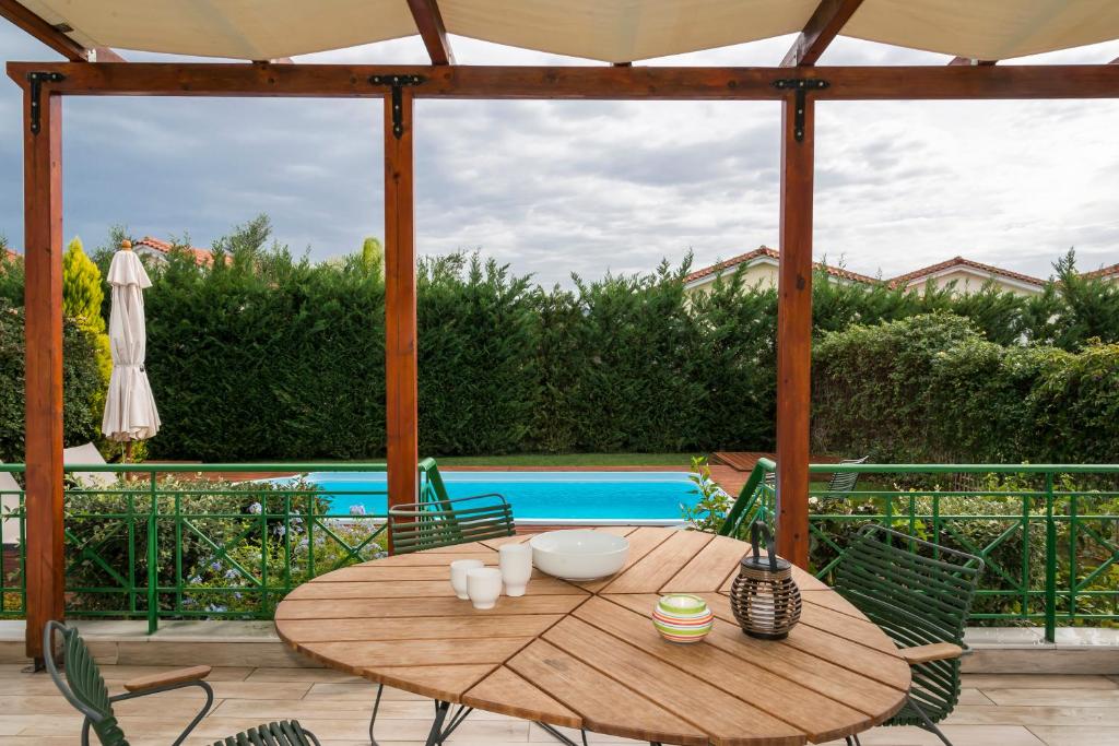 a wooden table and chairs on a patio with a pool at Venus Villa with Private Pool, 2min to the Beach in Finikounta