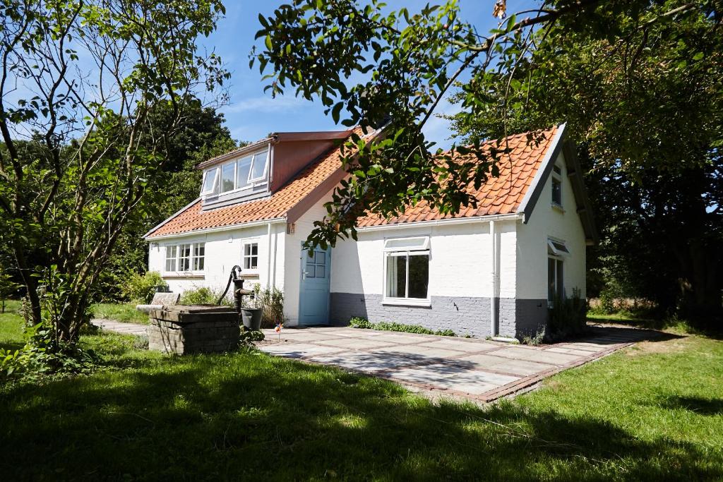 una pequeña casa blanca con techo rojo en Cottage Duinroos - Dune Rose, en Oostvoorne