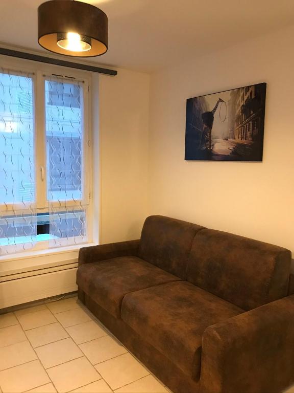 - un canapé brun dans le salon avec une fenêtre dans l&#39;établissement la licorne { T2 tous confort} centre ville, à Pont-Audemer