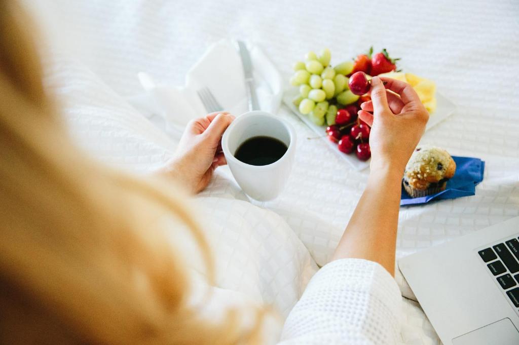 a person laying in bed with a cup of coffee and fruit at Hotel Indigo Orange Beach - Gulf Shores by IHG in Gulf Shores