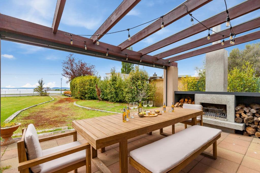 a patio with a wooden table and chairs and a fireplace at Waters Edge Retreat - Motuoapa Holiday Home in Turangi