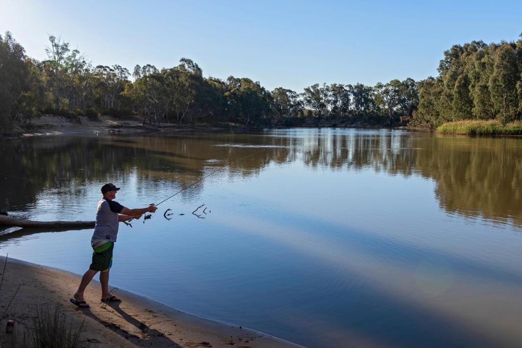 a man is standing on the shore of a lake fishing at Discovery Parks - Echuca in Echuca