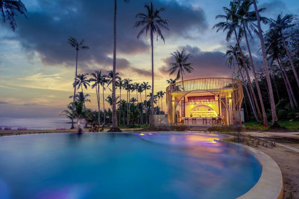 a swimming pool in front of a building with palm trees at Hideout Koh Kood in Ko Kood