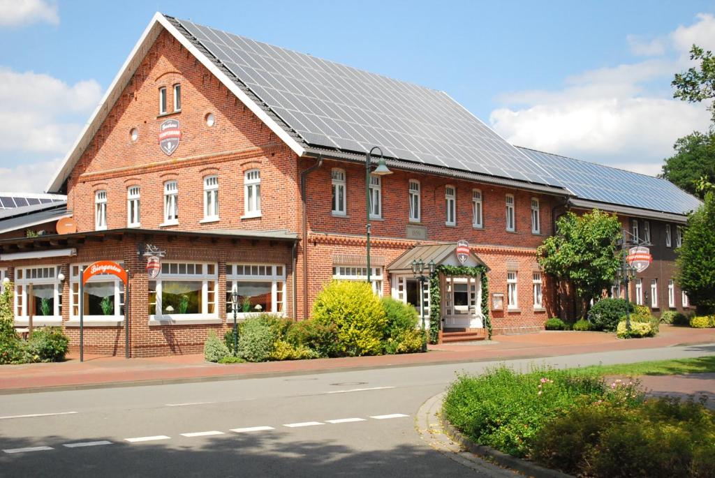 un grand bâtiment en briques rouges avec un toit noir dans l'établissement Gasthaus Kempermann, à Großenkneten