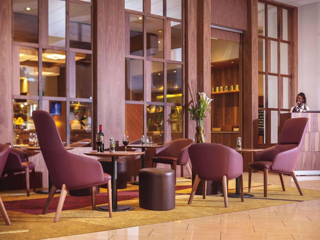 um restaurante com cadeiras e mesas e uma mulher ao fundo em Mövenpick Hotel Zürich-Regensdorf em Regensdorf