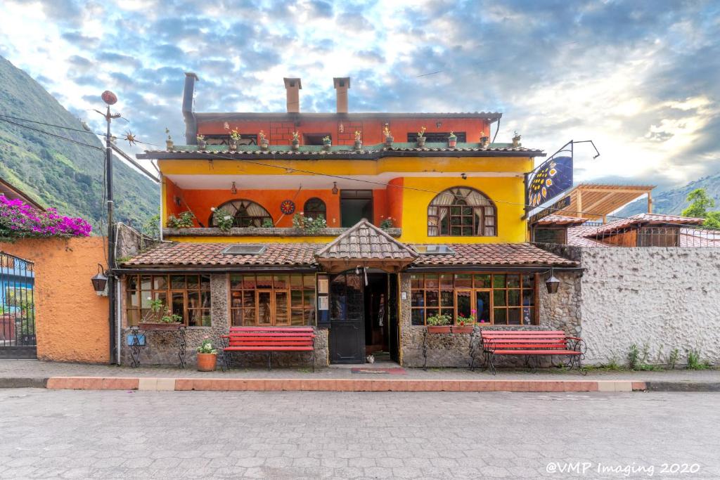 un edificio amarillo con dos bancos delante en La Posada Del Arte, en Baños