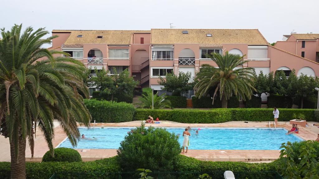 a large swimming pool with palm trees and buildings at LES SOLEILLADES Parking 200 mètres plage in Marsillargues