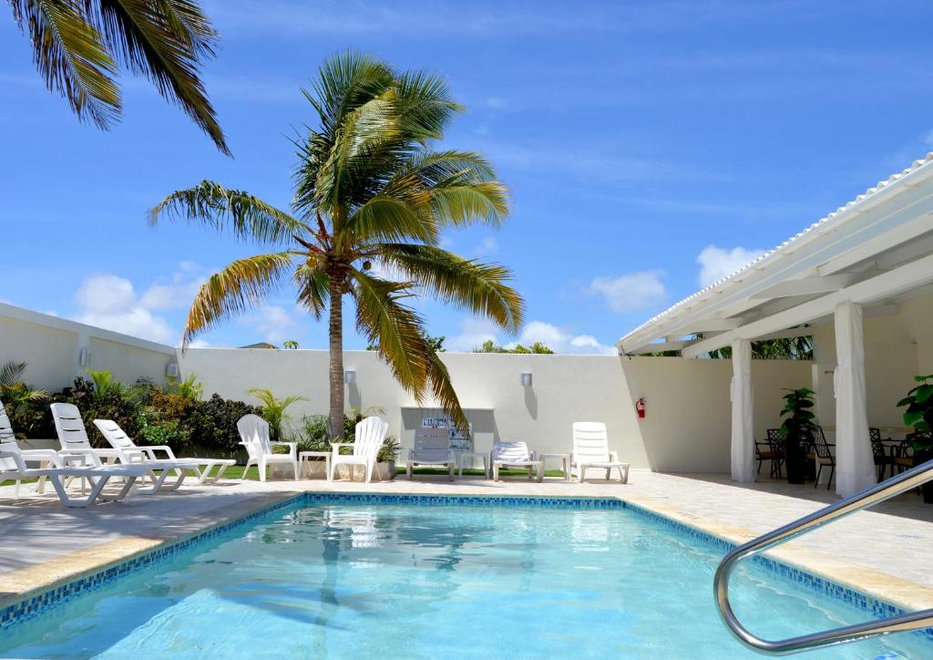 a swimming pool with chairs and a palm tree at Yoyita Suites Aruba Villa in Palm-Eagle Beach