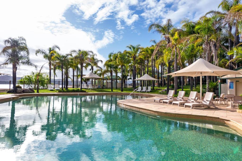 a swimming pool with chairs and umbrellas and palm trees at Discovery Parks - Lake Hume, Victoria in Bonegilla