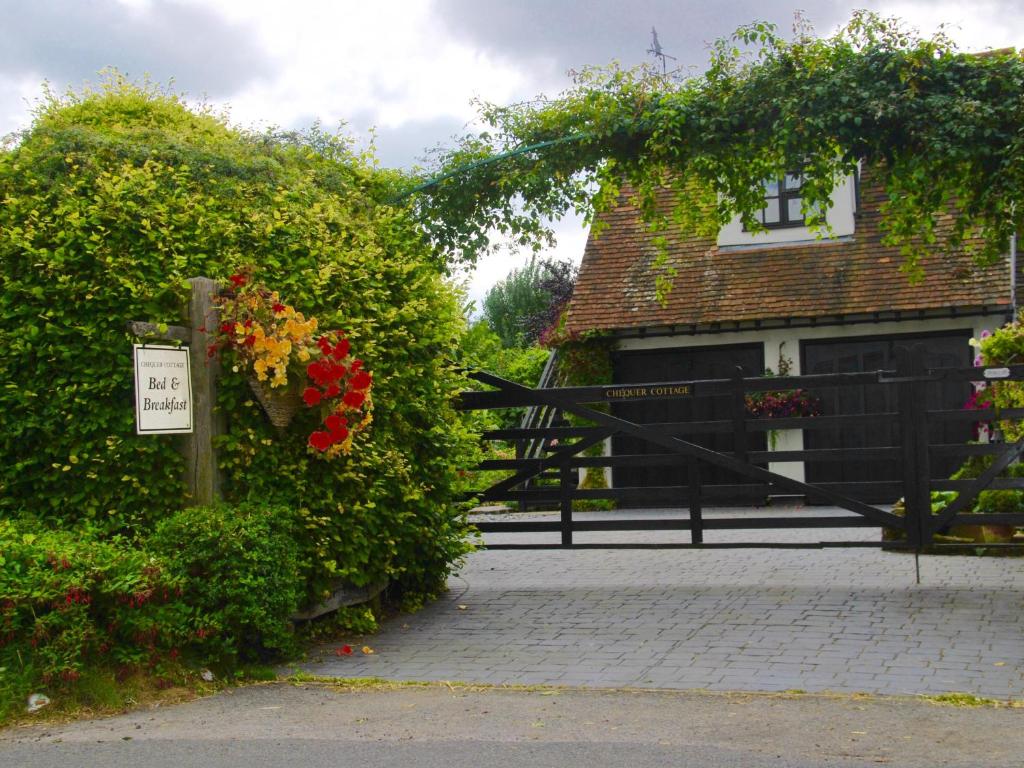 una casa con una puerta y algunos arbustos y flores en Chequer Cottage, en Horseheath