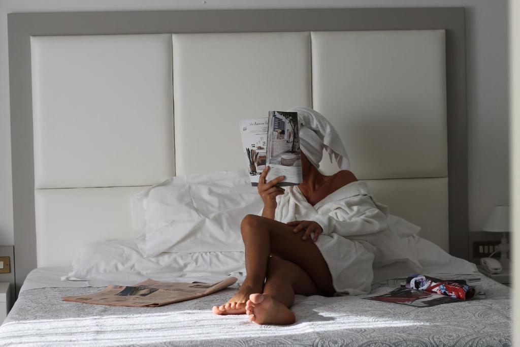 a woman sitting on a bed reading a magazine at Terme Villa Pace in Abano Terme