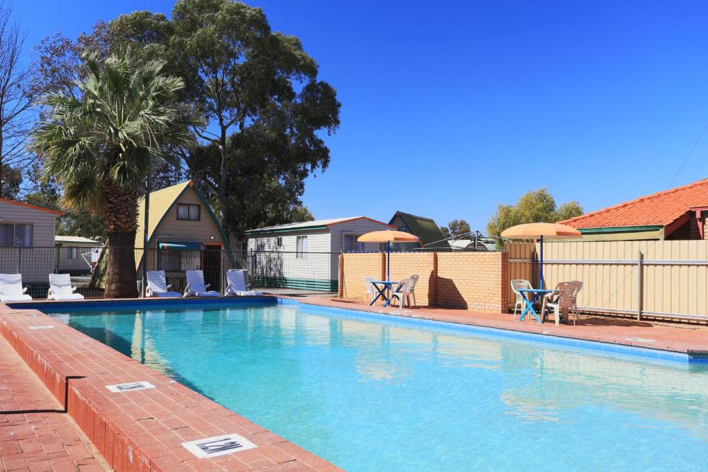 a swimming pool with chairs and umbrellas next to a house at Discovery Parks - Kalgoorlie Goldfields in Kalgoorlie