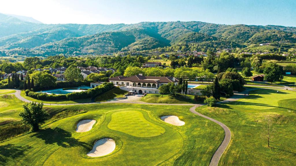 Asolo Golf Club في Cavaso del Tomba: اطلالة جوية على ملعب قولف مع جبال في الخلفية