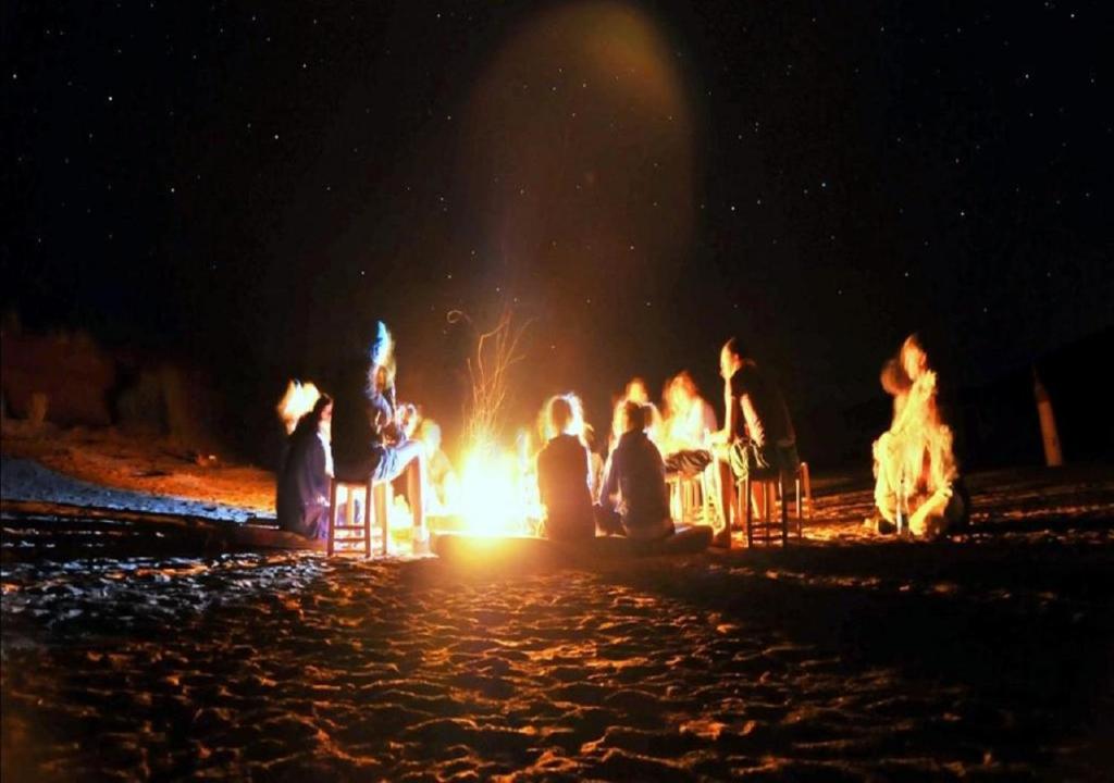 a group of people sitting around a fire at night at M'hamid Desert Camp Tours in Mhamid