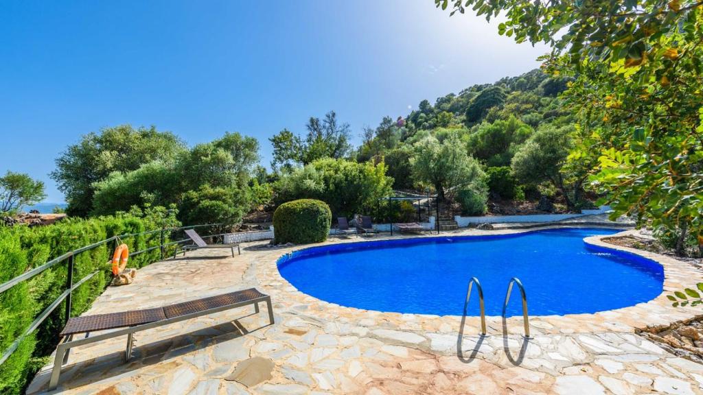 a large blue swimming pool with a bench and trees at Casa El Paraiso Escondido Montecorto by Ruralidays in Montecorto