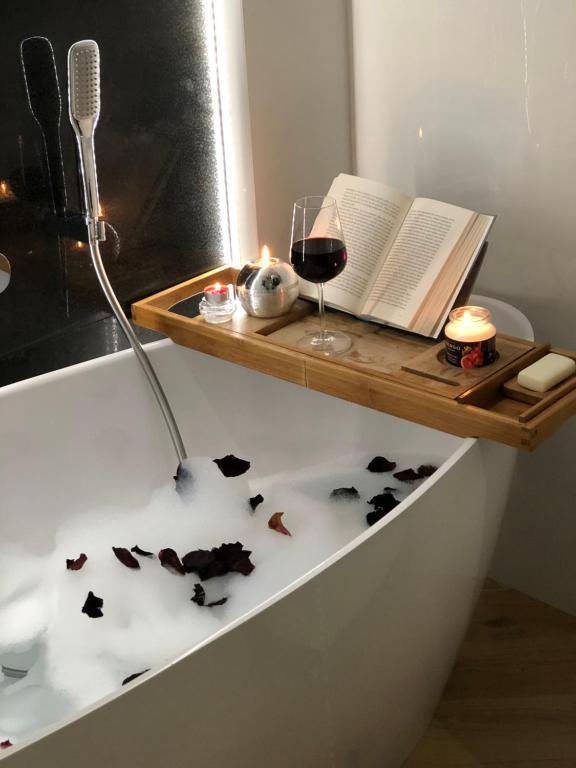 a bath tub with a book and a glass of wine at Apartament Primavera z sauną in Kielce