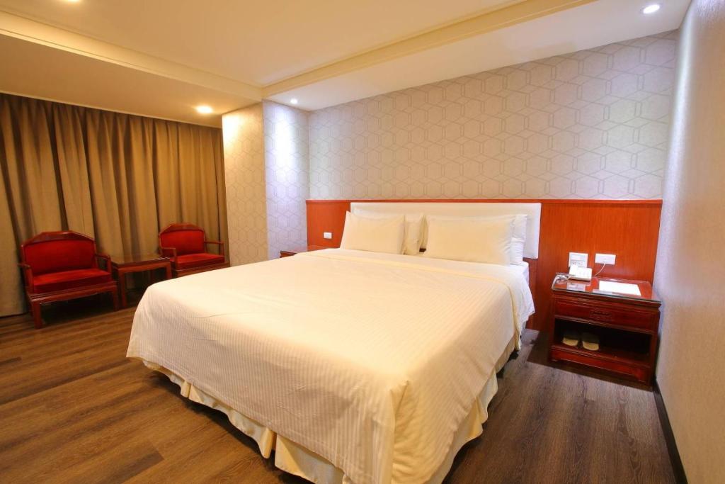una habitación de hotel con una gran cama blanca y sillas rojas en Chuan Fu Hotel en Fengyuan