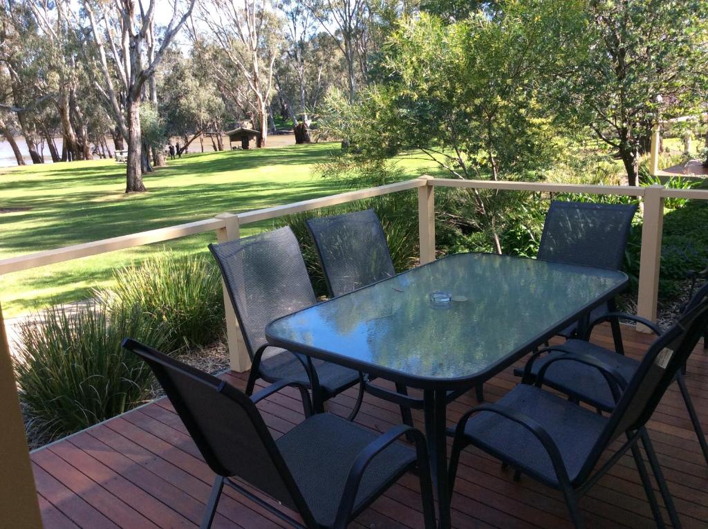 a glass table and chairs on a deck with a field at Winbi River Resort Holiday Rentals in Moama