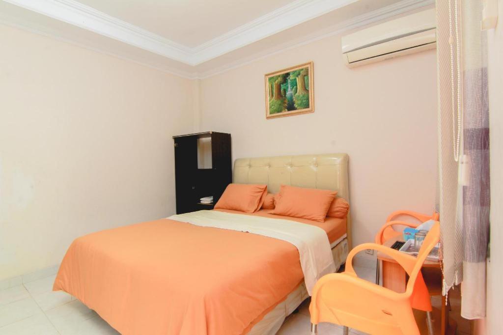 1 dormitorio con 1 cama con sábanas de color naranja y silla en Sabana Homestay, en Yogyakarta