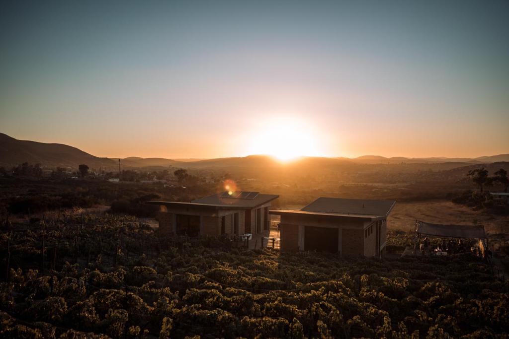 a house in a field with the sunset in the background at UvaUva eco-retreat in Valle de Guadalupe