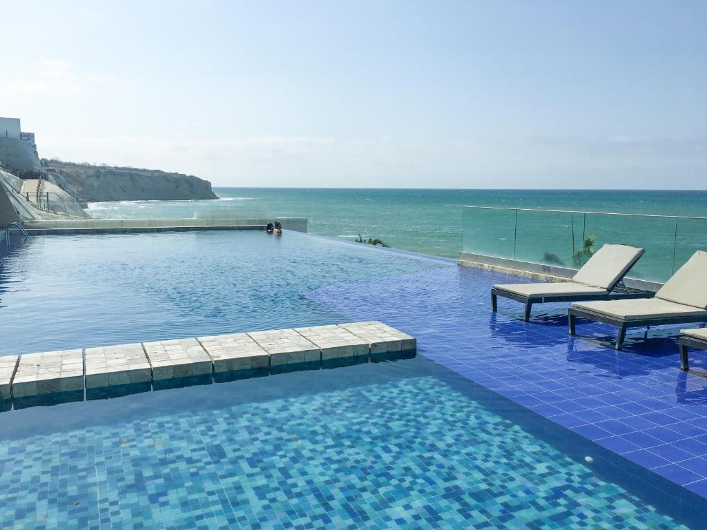 una piscina con 2 sillas y el océano en P2 Poseidon 5 Stars Ocean View Prestigioso Apartamento 2 Dormitorios, en Manta