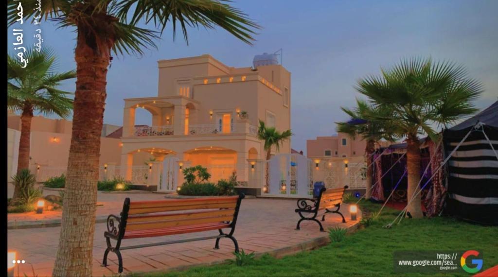 two benches in front of a house with palm trees at منتجع القصر الأبيض in Unayzah