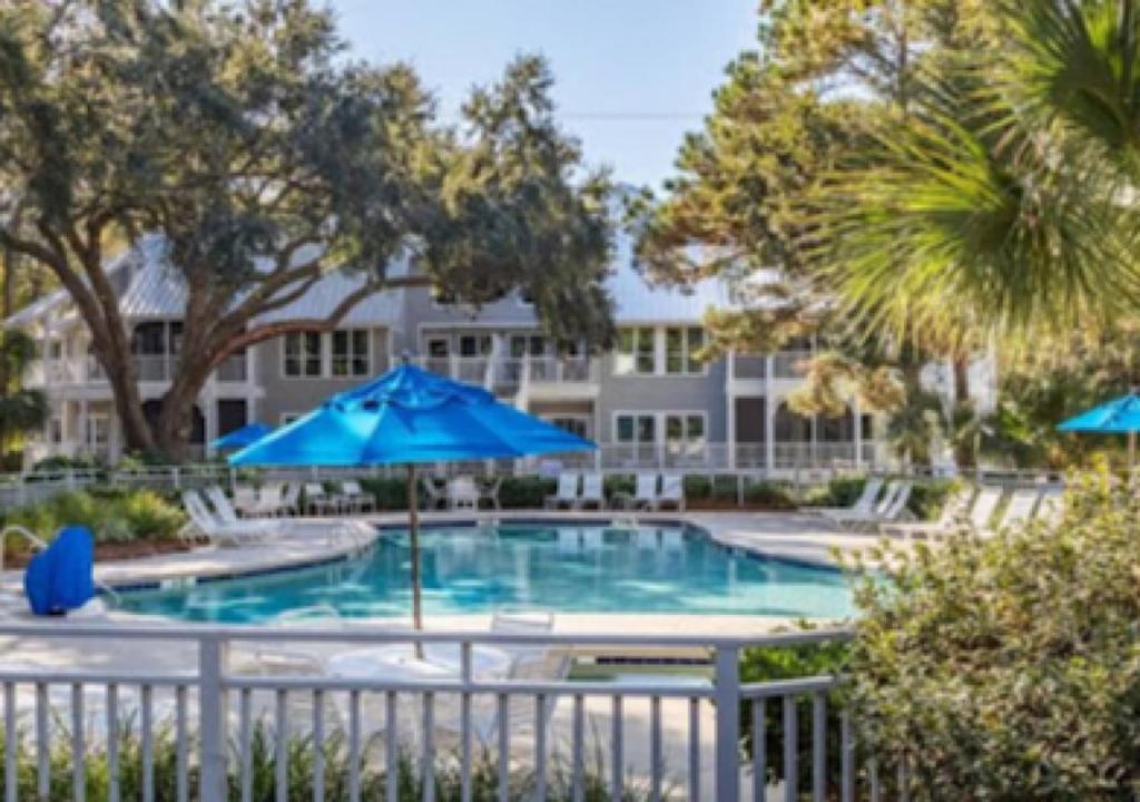 a pool with blue umbrellas in front of a building at Ocean Palms Villa with Championship Golf Saturday to Saturday Rental in Hilton Head Island