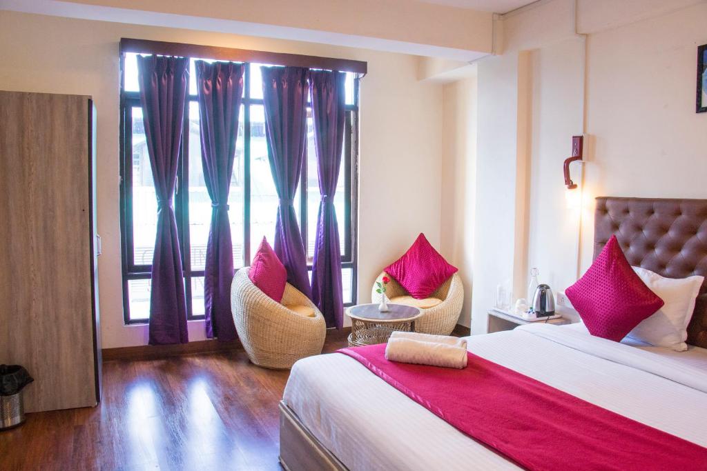 a bedroom with a bed and two chairs and a window at Humro Himalayan Orchid in Darjeeling