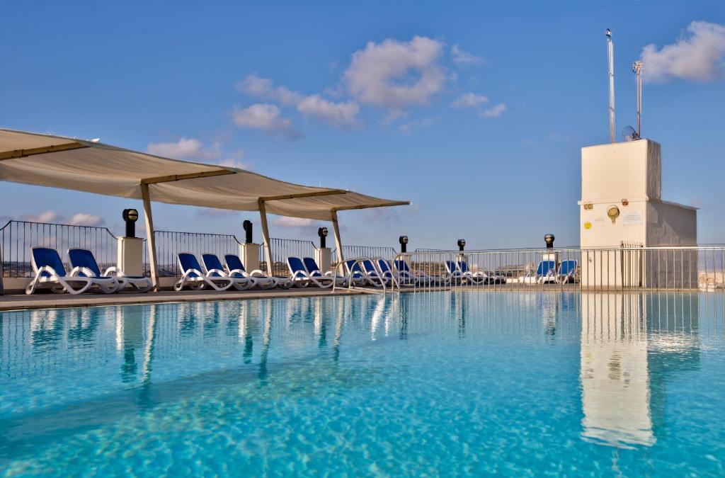 a swimming pool with chairs and umbrellas on a building at Hotel Santana in St Paul's Bay