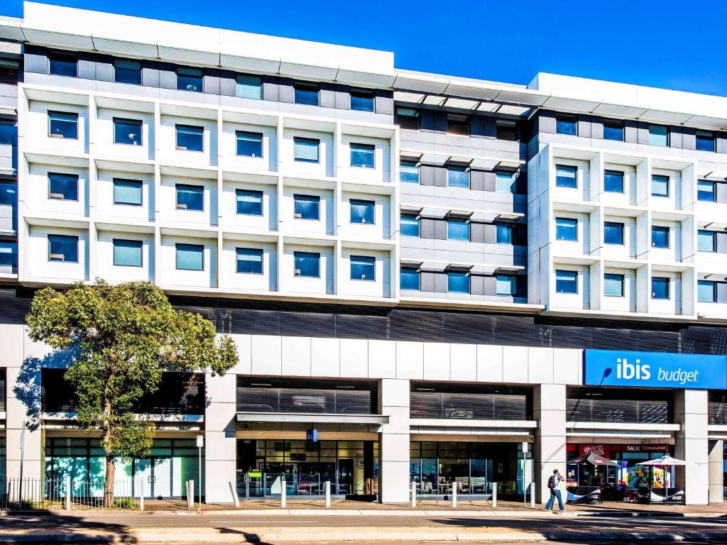 a large white building with a blue sign on it at ibis Budget Sydney Olympic Park in Sydney