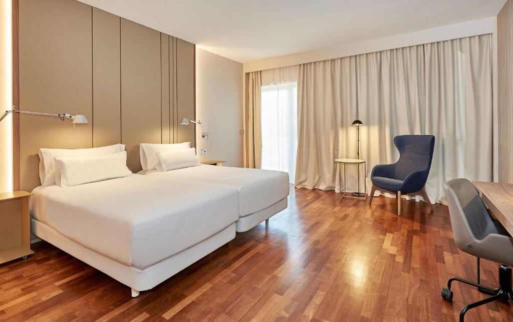 a bedroom with a large white bed and a blue chair at NH Luz Huelva in Huelva