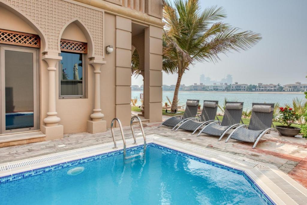 a swimming pool with chairs next to a house at Stella Stays Breathtaking 4BDR Palm Villa Beach Private Pool in Dubai